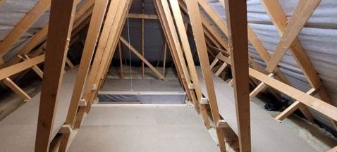 A symmetrical loft with a boarded walkway between trusses and the hatch opening visible
