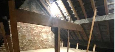 A boarded loft floor under a large timber beam, with brick gable and roof window