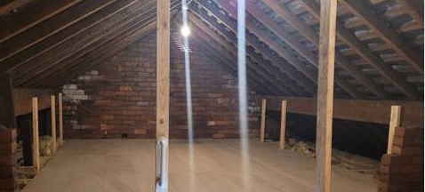 A long boarded loft with brick gable, pendant light and insulation at the edges